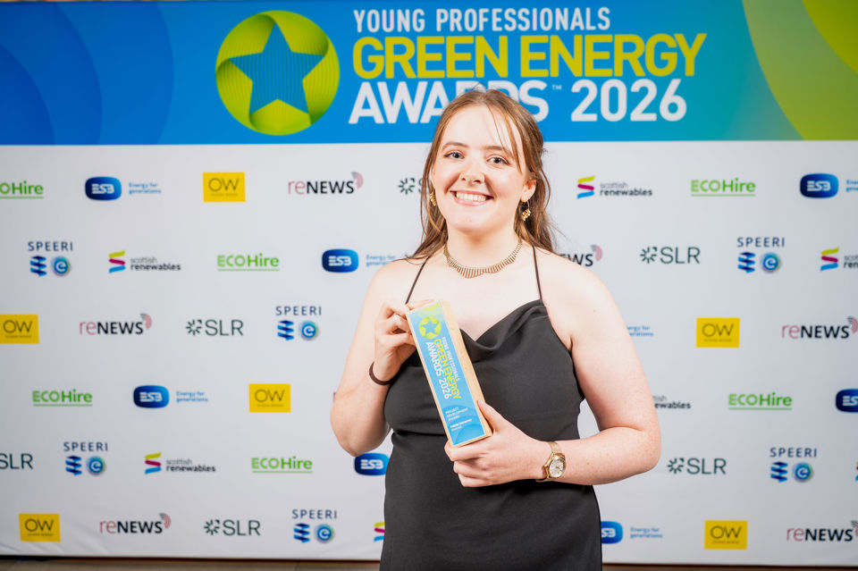 Photograph of a Felicity Devanney holding a Young Professionals Green Energy Awards 2026 trophy, standing in front of a branded backdrop featuring logos of sponsors and partners. The backdrop includes a prominent green and blue logo with a star.